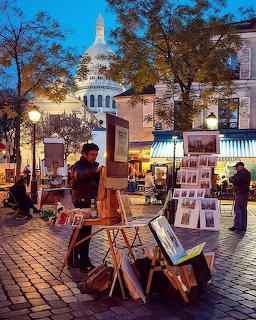 Street artists with paintings on easels in Montmartre square at twilight with illuminated Sacré-Cœur basilica behind