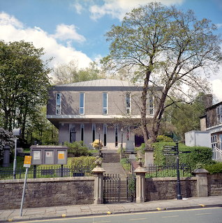 Gray stone Unitarian church with columned entrance, trees, and iron fence gate under blue sky