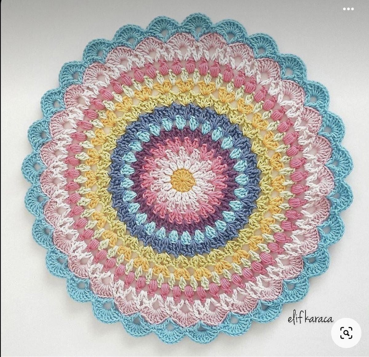Colorful crocheted mandala doily with concentric rainbow rings and scalloped lace border on white background