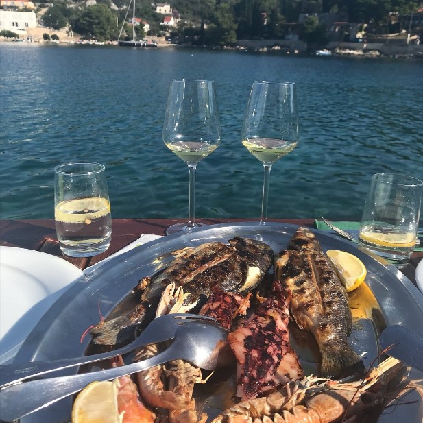 Grilled octopus platter with white wine glasses on table by blue sea