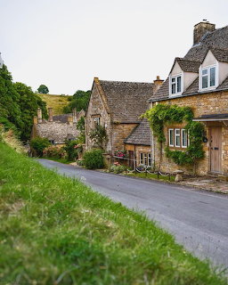 Row of traditional stone cottages along a village street with green lawns and hills