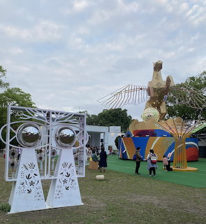 Outdoor park with large colorful abstract sculptures and decorative white art panels on grass under cloudy sky