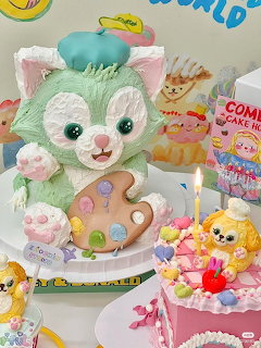 Pink decorated cake with a green cat character topper, candles, and colorful sweets