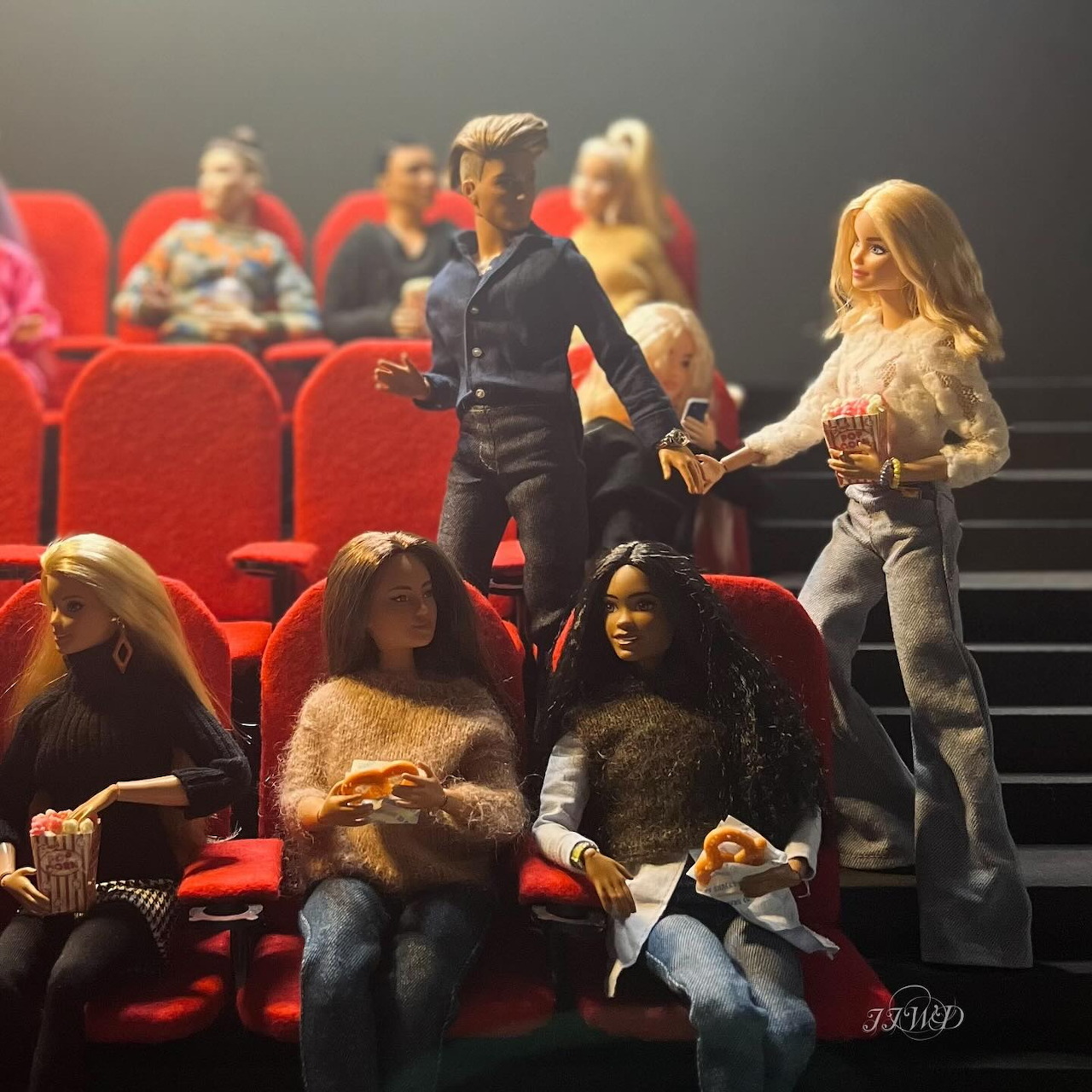 Barbie dolls in fashionable outfits sitting in red movie theater seats