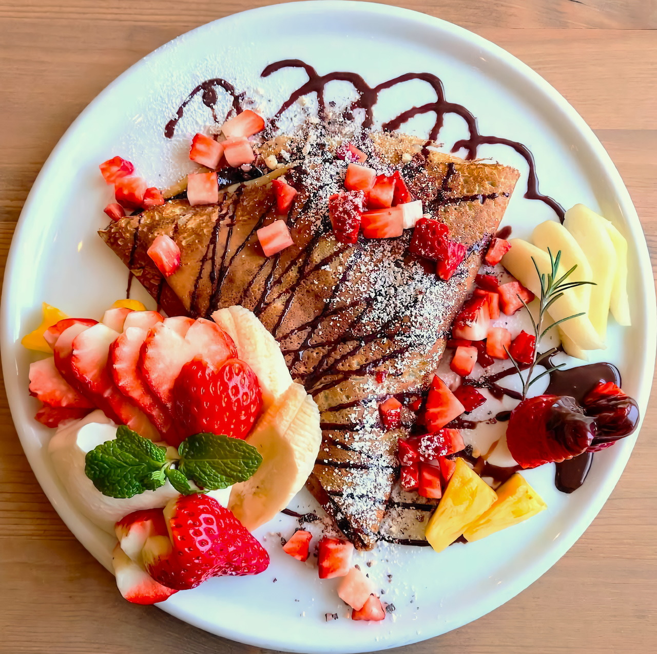 Crepe with strawberries, chocolate drizzle, whipped cream, and fruit on a white plate