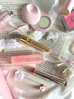 Pink makeup products and ribbons arranged on open book pages in a feminine coquette flatlay