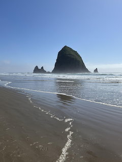 Haystack Rock and sea stacks at Cannon Beach Oregon with waves on sandy shore under blue sky