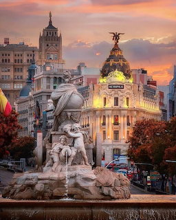 Madrid Metropolis building at sunset with Cibeles fountain statue, illuminated dome and pink-orange sky