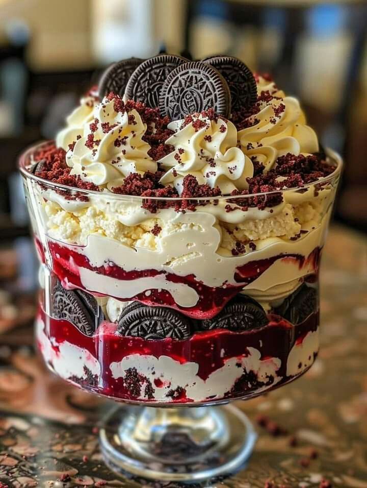 Oreo sundae in a glass dish with whipped cream, cookie crumbs, and red berry sauce