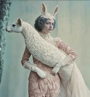 Woman in rabbit ears and lace dress holding a white alpaca in a vintage portrait style