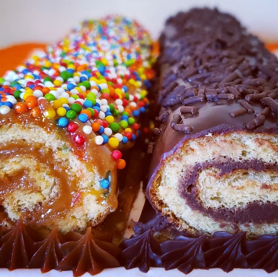 Two sliced cake rolls on orange plate, one with rainbow sprinkles, one chocolate-covered with hazelnuts