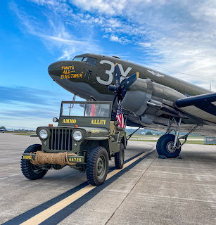 Vintage military jeep beside a World War II warplane under blue sky