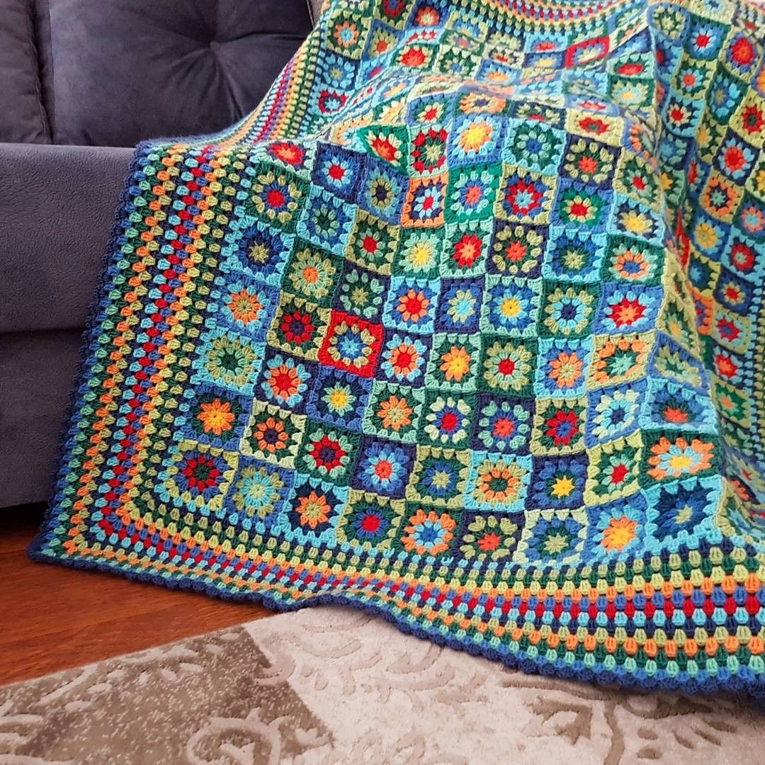 Colorful crocheted granny square blanket with floral pattern on gray couch