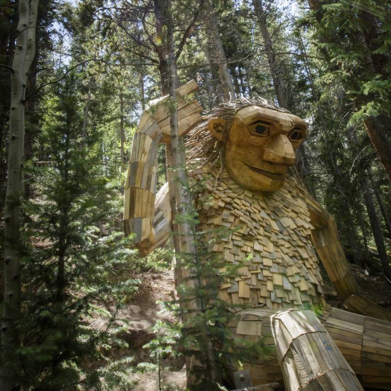 Large wooden troll sculpture in a forest of tall pine trees