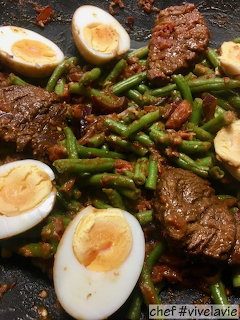 Sambal goreng telor with halved boiled eggs, green beans, and beef in red chili sauce on dark plate