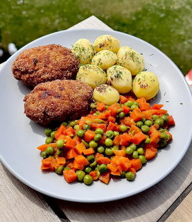 Plate with two breaded cutlets, boiled potatoes, and colorful mixed vegetables on outdoor table