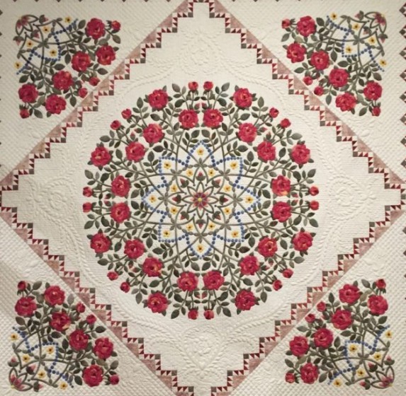 Vintage quilt with red roses in circular medallion pattern on cream background with decorative stitching