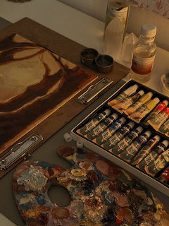 Artist's desk with paint tubes in a tin, colorful palette, and canvas with brown swirled paint