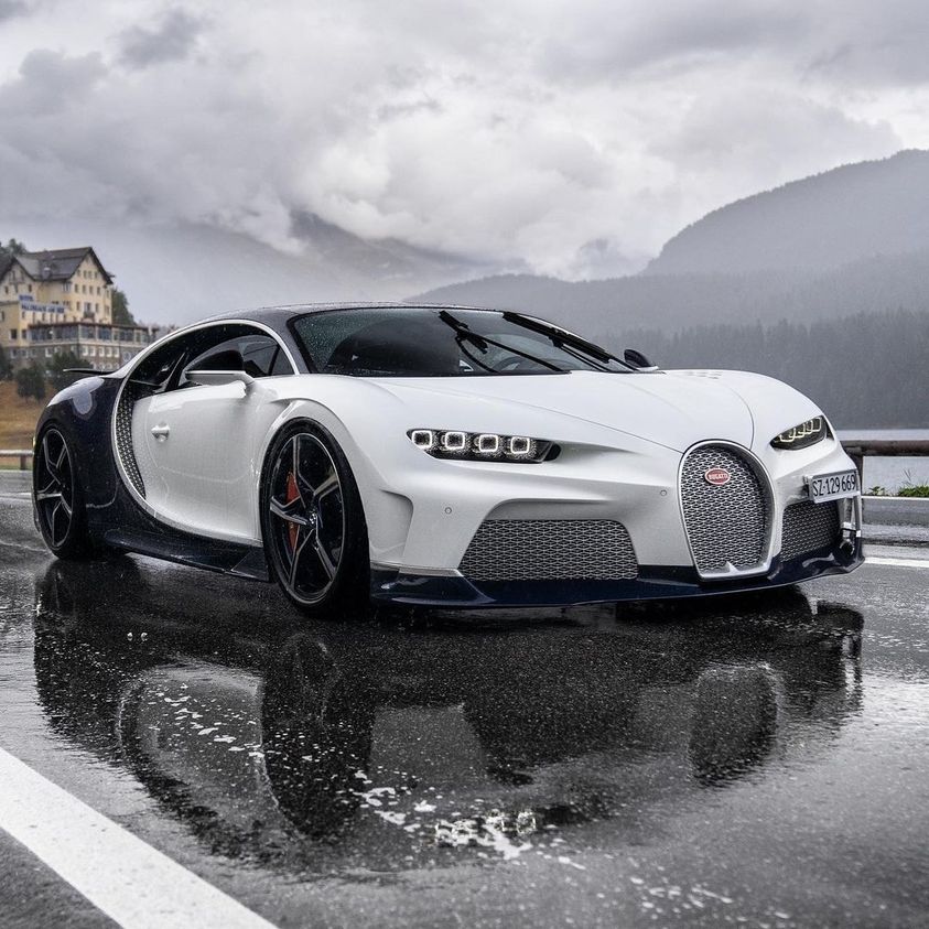 White Bugatti Chiron on a rain-soaked road with mountain scenery and cloudy sky