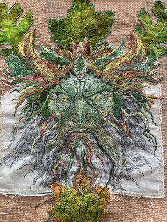 Embroidered Green Man face with oak leaves and flowing beard in green and earth tones on fabric