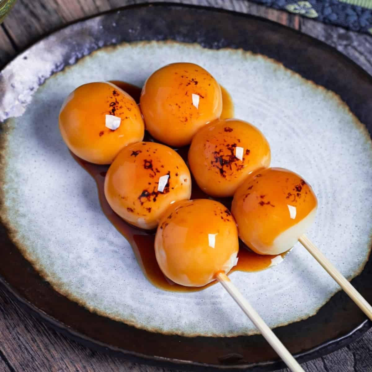 Two skewers of glazed Japanese dango dumplings on a white ceramic plate with dark rim