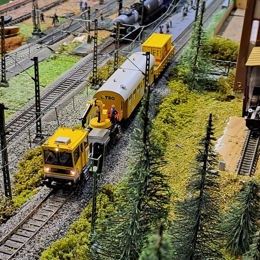 Yellow model maintenance train on tracks in a miniature railway landscape