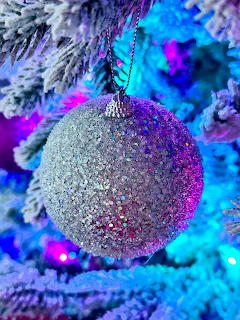 Glittery silver Christmas ball ornament on a flocked tree with colorful lights