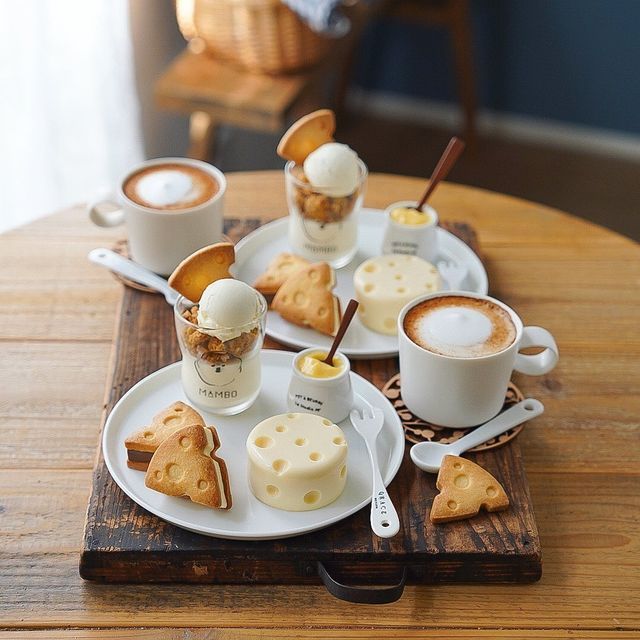 Cappuccinos and small desserts on white plates arranged on a wooden cafe table indoors