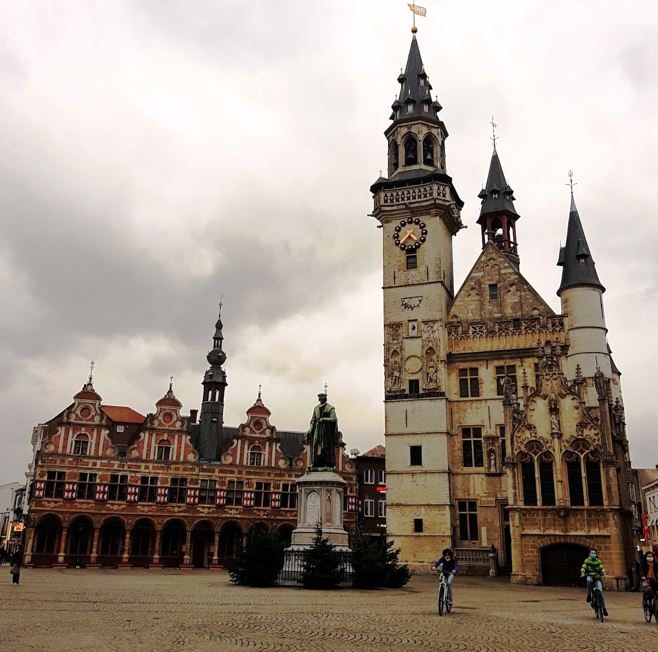 Historic town square with ornate buildings, statue, and tall clock tower in Aalst, Belgium