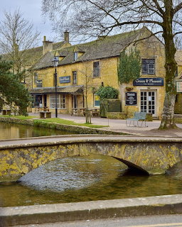 Stone bridge over stream with traditional Cotswold buildings and bare trees in English village