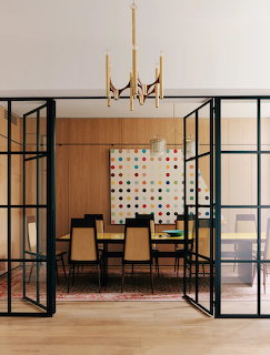 Modern dining room with black steel-framed glass doors, polka dot wall art, brass chandelier and wooden table