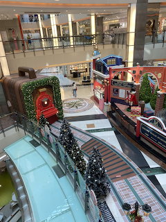 Shopping mall interior with Christmas decorations, train display, trees, and escalator viewed from above