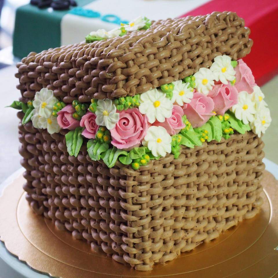 Basket-shaped cake with woven frosting, pink roses, and white daisy flowers
