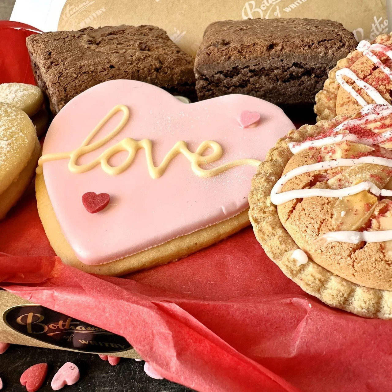 Pink heart cookie with love icing surrounded by assorted cookies and pastries