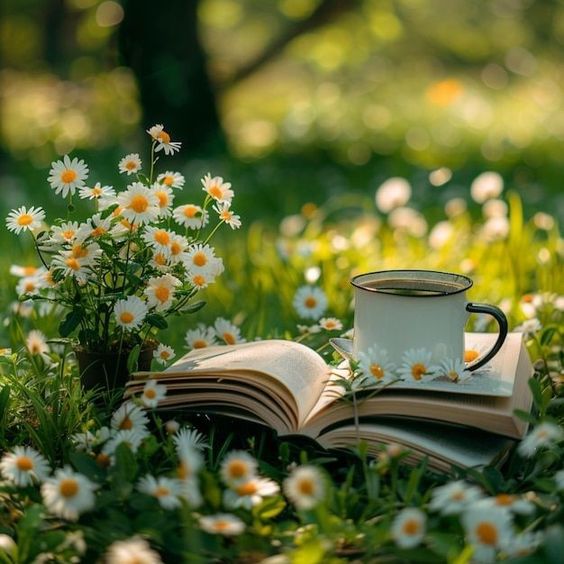 White enamel coffee mug on open book surrounded by white daisies in garden