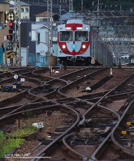Red and white commuter train on multiple railway tracks with signal equipment and overhead wires