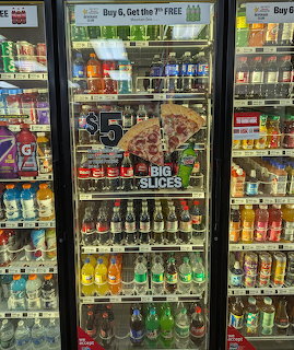 Glass-door store refrigerators stocked with soft drinks, water, and a pizza advertisement