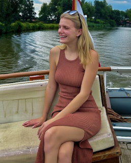 Smiling blonde woman in a brown sleeveless dress sitting on a boat by a river