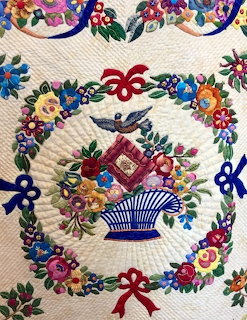 Quilted cream fabric with a blue basket, flowers, and a colorful floral wreath pattern
