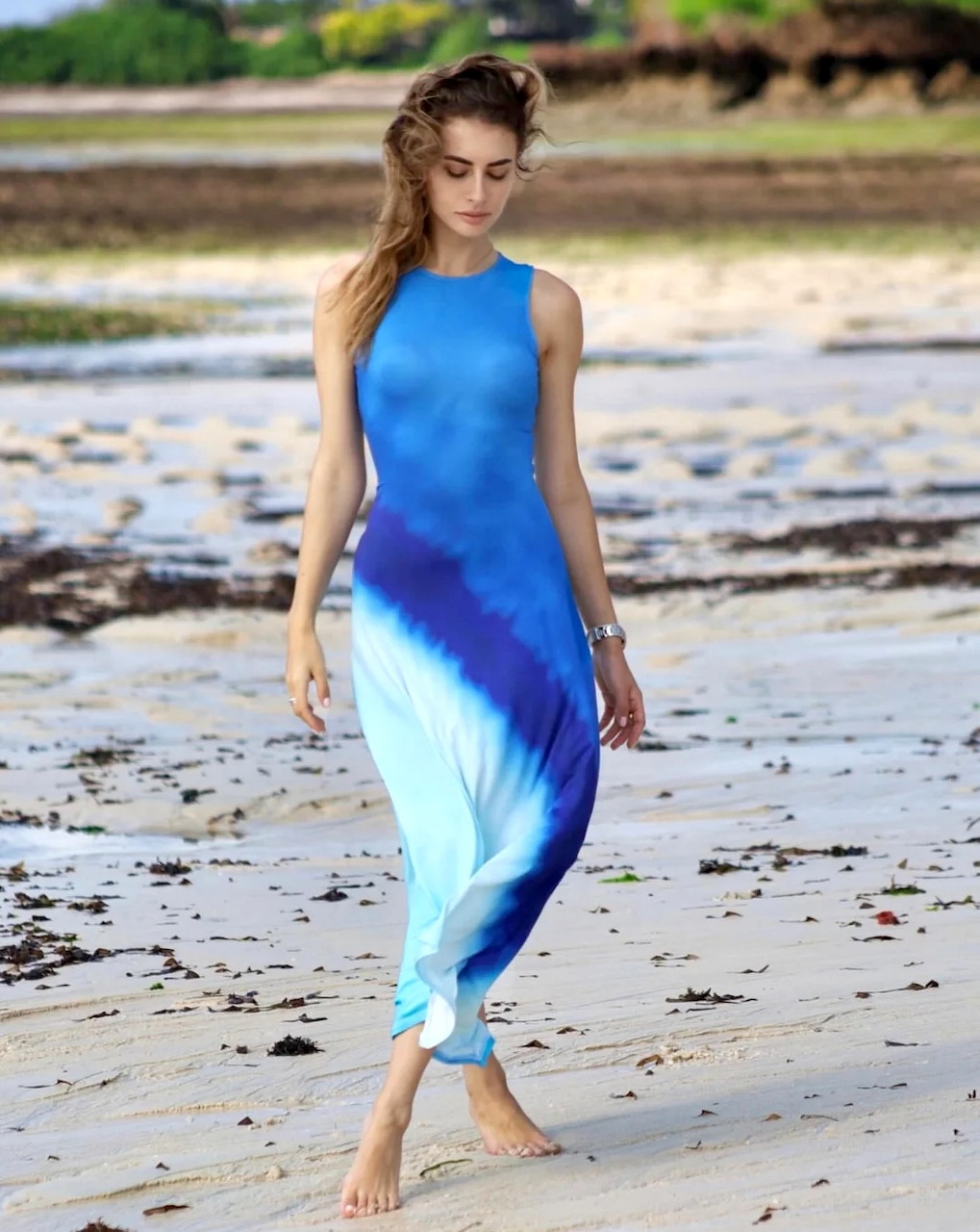 Woman in elegant blue ombre dress walking barefoot on beach