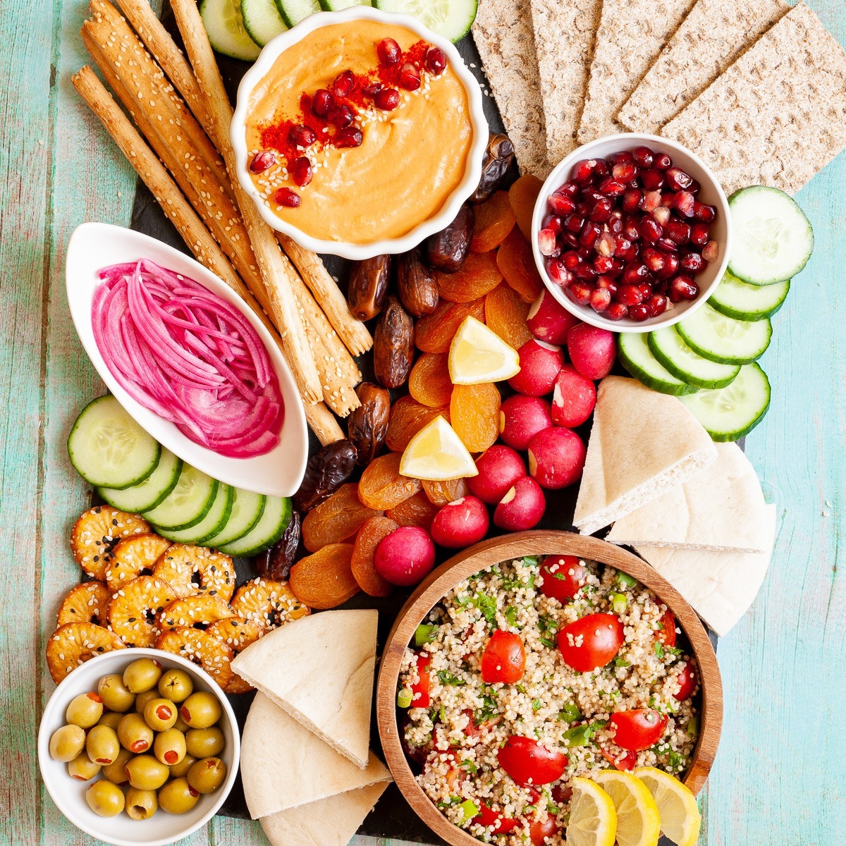 Overhead shot of a colorful cheese and charcuterie board with fresh vegetables, crackers, dips, and salads
