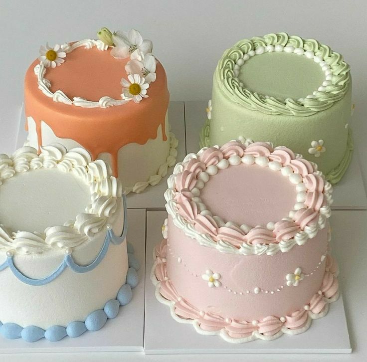Four pastel decorated cakes with piped icing and small floral details on white stands