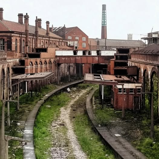 Abandoned brick factory buildings with a curved overgrown track and industrial chimney