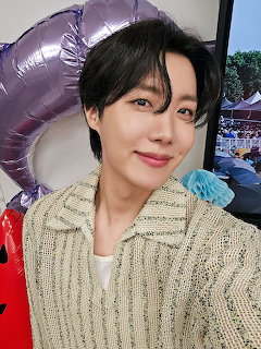 Close-up selfie of a smiling young man indoors with balloons behind him