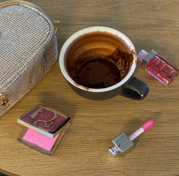 Coffee cup with lipstick and cosmetics on wooden surface