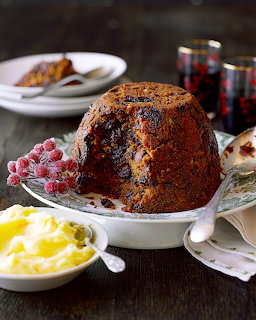 Traditional Christmas pudding topped with sugared cranberries on a white plate with cream on the side