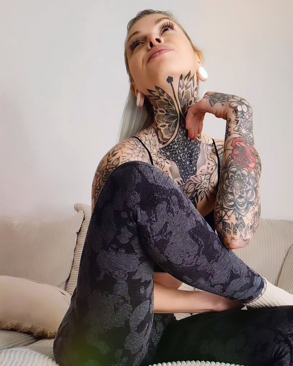 Tattooed woman in lace dress sitting on couch with head tilted back