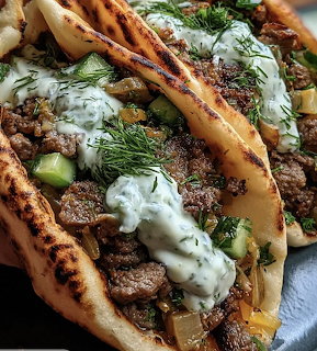 Close-up of grilled beef tacos with creamy herb sauce, diced cucumber, and fresh dill