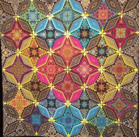 Colorful handmade quilt with repeating star pattern in multiple bright colors on dark background