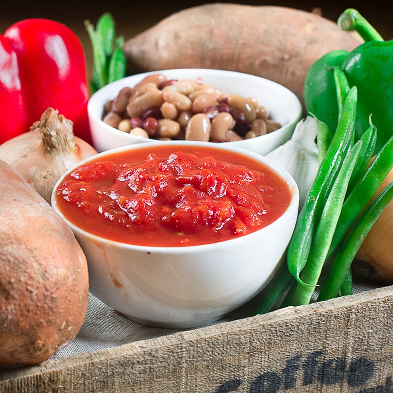 Fresh vegetables, legumes, and tomato sauce arranged on burlap with white bowls